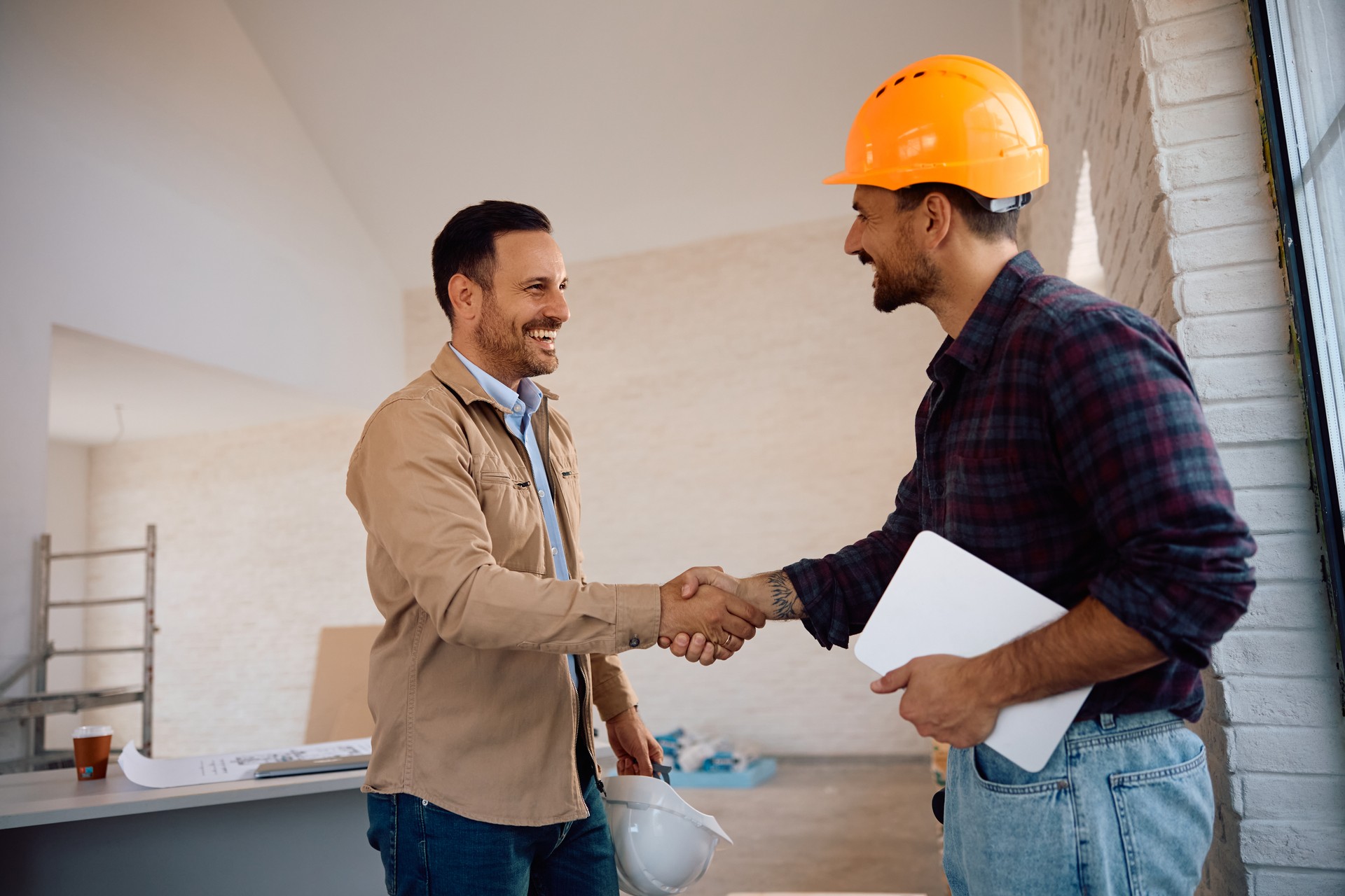 Happy home owner and construction site worker handshaking at renovating house.